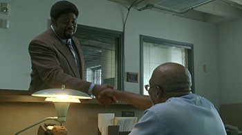 Movie still from “Roll Bounce” (2005), directed by Malcolm D. Lee – Two men shaking hands in an office setting; Medium shot, Over the shoulder angle