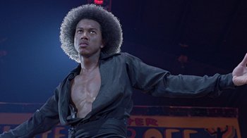 Movie still from “Roll Bounce” (2005), directed by Malcolm D. Lee – A man in a black shirt and a black jacket is on a stage; Close Up shot, Low angle