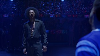 Movie still from “Roll Bounce” (2005), directed by Malcolm D. Lee – A man in a black shirt is standing in a dark room; Medium shot, Low angle