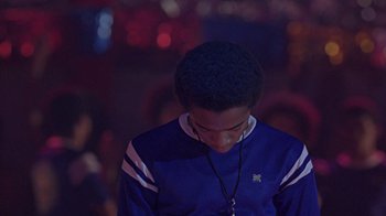 Movie still from “Roll Bounce” (2005), directed by Malcolm D. Lee – A person with a blue shirt is listening to music; Medium shot, Over the shoulder angle