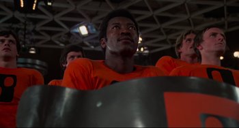 Movie still from “Rollerball” (1975), directed by Norman Jewison – A group of men in orange shirts looking up; Close Up shot, Low angle