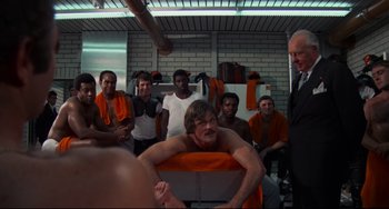 Movie still from “Rollerball” (1975), directed by Norman Jewison – A group of people in a room with a man in the background; Medium shot, Low angle