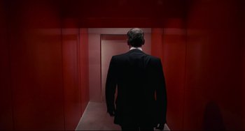 Movie still from “Rollerball” (1975), directed by Norman Jewison – A man wearing a suit and tie walking down a red hallway; Medium shot, Low angle