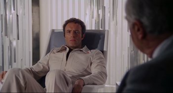 Movie still from “Rollerball” (1975), directed by Norman Jewison – A man sitting in a chair in front of another man; Medium shot, Over the shoulder angle