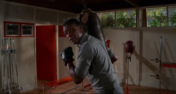 Movie still from “Rollerball” (1975), directed by Norman Jewison – A man in grey shirt and boxing gloves in a gym; Medium shot, Low angle
