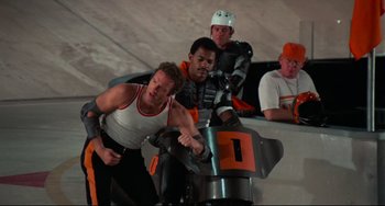 Movie still from “Rollerball” (1975), directed by Norman Jewison – A group of men riding a motorcycle in a parking lot; Wide shot, Low angle