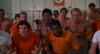 Movie still from “Rollerball” (1975), directed by Norman Jewison – A group of men in orange shirts are posing for a picture; Medium shot, Low angle