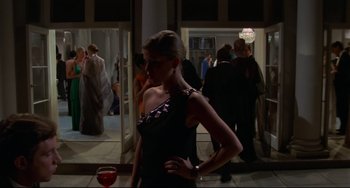 Movie still from “Rollerball” (1975), directed by Norman Jewison – A woman in a black dress standing next to a glass of red wine; Medium shot, Low angle