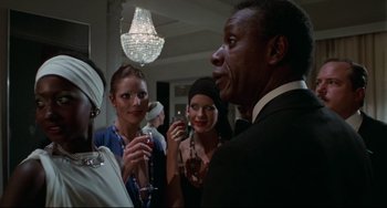 Movie still from “Rollerball” (1975), directed by Norman Jewison – A group of people standing in a room with wine glasses; Medium shot, Over the shoulder angle