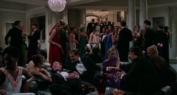 Movie still from “Rollerball” (1975), directed by Norman Jewison – A group of people in formal wear sitting on couches in a living room; Wide shot, High angle