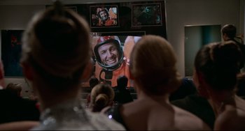 Movie still from “Rollerball” (1975), directed by Norman Jewison – Two people watching a television screen with a picture of a man in a helmet on it; Medium shot, Over the shoulder angle
