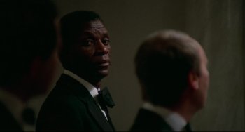 Movie still from “Rollerball” (1975), directed by Norman Jewison – A man in a suit and bow tie looking at another man in a suit and bow tie; Close Up shot, Over the shoulder angle