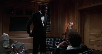 Movie still from “Rollerball” (1975), directed by Norman Jewison – A man in a tuxedo standing in front of another man in a suit; Medium shot, Low angle