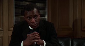 Movie still from “Rollerball” (1975), directed by Norman Jewison – A man wearing a suit and tie sitting in a chair; Close Up shot, Low angle