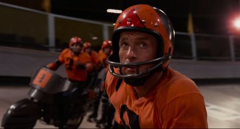 Movie still from “Rollerball” (1975), directed by Norman Jewison – A group of men riding on a bike in orange uniforms; Close Up shot, Low angle