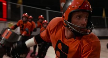 Movie still from “Rollerball” (1975), directed by Norman Jewison – A group of men in orange shirts and helmets playing a game; Close Up shot, Low angle