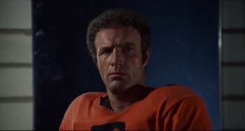 Movie still from “Rollerball” (1975), directed by Norman Jewison – A person wearing an orange shirt; Close Up shot, Low angle