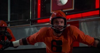 Movie still from “Rollerball” (1975), directed by Norman Jewison – A man wearing a helmet and a orange shirt; Medium shot, Low angle