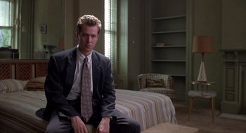 Movie still from “Romeo Is Bleeding” (1993), directed by Peter Medak – A man in a suit sitting on a chair in front of a bed; Medium shot, Low angle