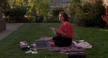 Movie still from “Romeo Is Bleeding” (1993), directed by Peter Medak – A woman sitting on a blanket in the grass; Wide shot, High angle