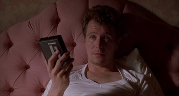 Movie still from “Romeo Is Bleeding” (1993), directed by Peter Medak – A man laying in a bed holding a cell phone; Close Up shot, Low angle