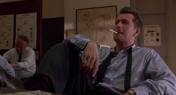 Movie still from “Romeo Is Bleeding” (1993), directed by Peter Medak – A man sitting on a couch with a cigarette in his mouth; Medium shot, Low angle