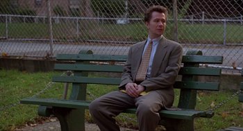 Movie still from “Romeo Is Bleeding” (1993), directed by Peter Medak – A man sitting on a green bench in a park; Medium shot, Low angle