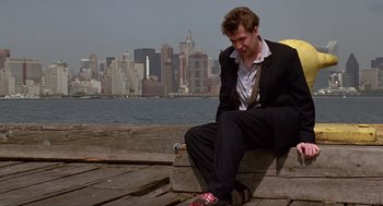Movie still from “Romeo Is Bleeding” (1993), directed by Peter Medak – A man sitting on a pier in front of a body of water; Wide shot, Low angle