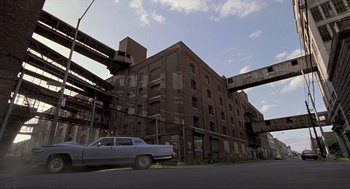 Movie still from “Romeo Is Bleeding” (1993), directed by Peter Medak – A car parked on the side of the road next to a building; Extreme Wide shot, High angle