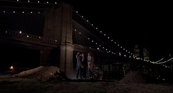 Movie still from “Romeo Is Bleeding” (1993), directed by Peter Medak – Three people standing in front of the brooklyn bridge at night; Extreme Wide shot, Low angle