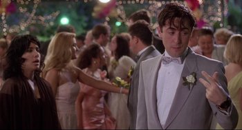 Movie still from “Romy and Michele's High School Reunion” (1997), directed by David Mirkin – A group of people in formal wear standing in a crowd; Medium shot, Over the shoulder angle