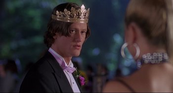 Movie still from “Romy and Michele's High School Reunion” (1997), directed by David Mirkin – A young man wearing a crown and a tuxedo; Medium shot, Over the shoulder angle
