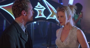 Movie still from “Romy and Michele's High School Reunion” (1997), directed by David Mirkin – A man and a woman are talking to each other in front of a neon sign; Medium shot, Over the shoulder angle