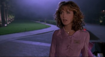 Movie still from “Romy and Michele's High School Reunion” (1997), directed by David Mirkin – A woman in a purple jacket standing on a sidewalk; Medium shot, Over the shoulder angle