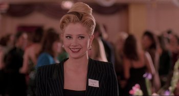 Movie still from “Romy and Michele's High School Reunion” (1997), directed by David Mirkin – A woman in a black suit smiling for the camera; Close Up shot, Over the shoulder angle