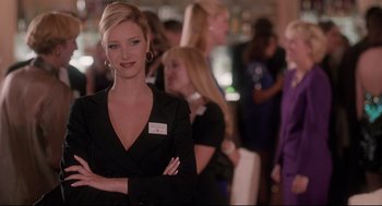 Movie still from “Romy and Michele's High School Reunion” (1997), directed by David Mirkin – A woman in a black suit and a white badge; Medium shot, Over the shoulder angle