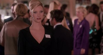 Movie still from “Romy and Michele's High School Reunion” (1997), directed by David Mirkin – A woman in a black dress standing in front of a group of people; Medium shot, Over the shoulder angle