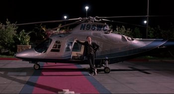 Movie still from “Romy and Michele's High School Reunion” (1997), directed by David Mirkin – A man standing in front of a helicopter at night; Wide shot, Low angle
