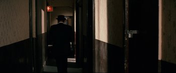 Movie still from “'Round Midnight” (1986), directed by Bertrand Tavernier – A man in a suit and top hat walking through a building; Wide shot, Over the shoulder angle