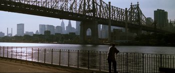 Movie still from “'Round Midnight” (1986), directed by Bertrand Tavernier – A man standing next to a body of water near a bridge; Extreme Wide shot, Over the shoulder angle