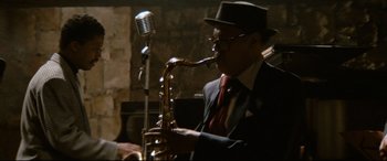 Movie still from “'Round Midnight” (1986), directed by Bertrand Tavernier – A man in a suit and hat playing a saxophone; Medium shot, Over the shoulder angle