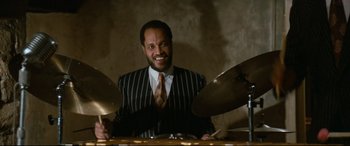 Movie still from “'Round Midnight” (1986), directed by Bertrand Tavernier – A man wearing a suit and tie sitting at a table; Medium shot, Low angle