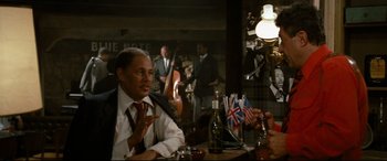 Movie still from “'Round Midnight” (1986), directed by Bertrand Tavernier – A man sitting at a table in front of a microphone; Medium shot, Over the shoulder angle