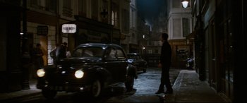 Movie still from “'Round Midnight” (1986), directed by Bertrand Tavernier – A man walking down the street with a car in front of him; Wide shot, Over the shoulder angle
