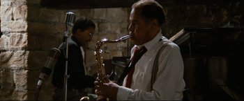 Movie still from “'Round Midnight” (1986), directed by Bertrand Tavernier – A man in a white dress shirt and a red tie playing a saxophone; Medium shot, High angle