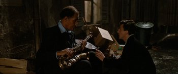 Movie still from “'Round Midnight” (1986), directed by Bertrand Tavernier – A man sitting next to another man holding a saxophone; Medium shot, High angle