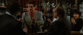 Movie still from “'Round Midnight” (1986), directed by Bertrand Tavernier – A man in a gray jacket is holding a bottle of wine; Medium shot, Over the shoulder angle