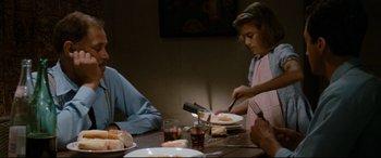 Movie still from “'Round Midnight” (1986), directed by Bertrand Tavernier – A woman cutting a pizza at a table with other people sitting around it; Medium shot, Over the shoulder angle