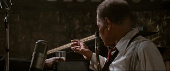 Movie still from “'Round Midnight” (1986), directed by Bertrand Tavernier – A man sitting at a table holding a glass of wine; Close Up shot, Over the shoulder angle