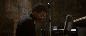 Movie still from “'Round Midnight” (1986), directed by Bertrand Tavernier – A man with glasses sitting in front of a microphone; Close Up shot, High angle